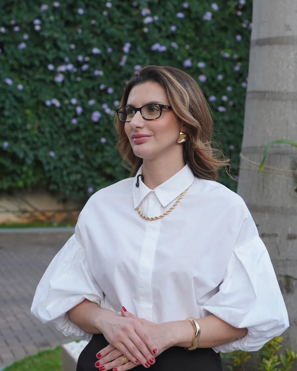 Dra. Bruna Benassi, de camisa branca, no jardim em frente ao consultório